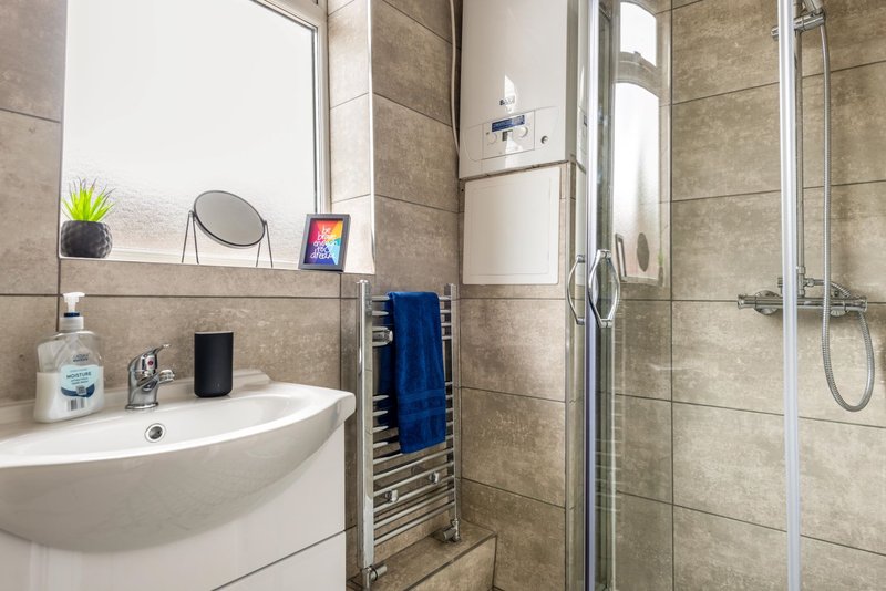 Modern bathroom with beige tile walls, white sink, mirror, towel rail and shower enclosure