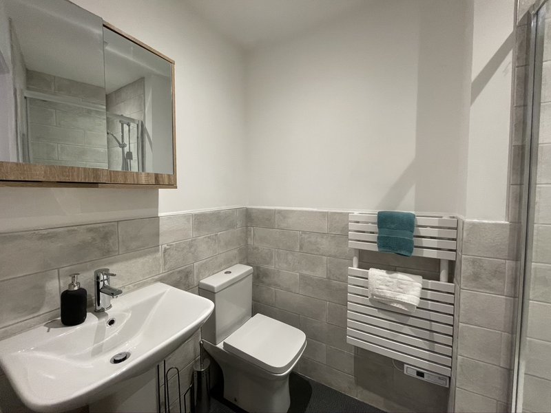 Modern bathroom with grey tile walls, white sink, toilet, mirror and heated towel rail