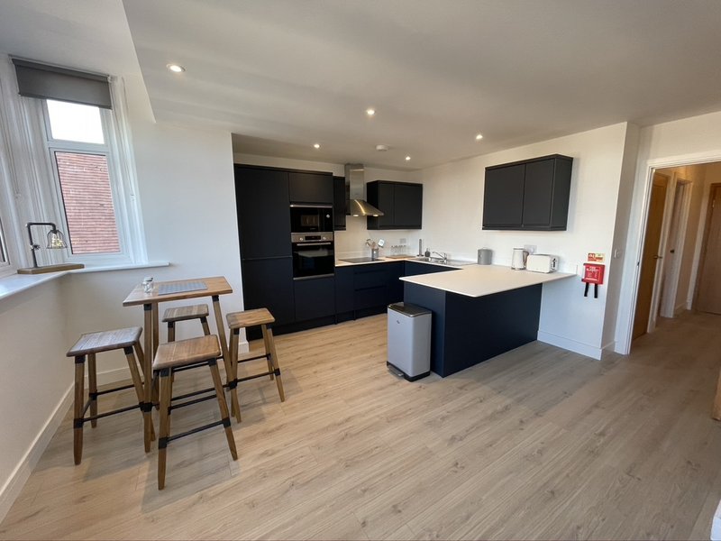 Modern open-plan kitchen and dining area with black cabinetry, island, wooden bar stools and hardwood flooring