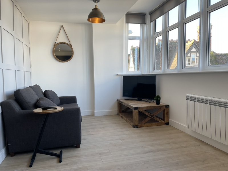 Living room with dark armchair, wooden TV stand, round mirror, pendant light and large windows