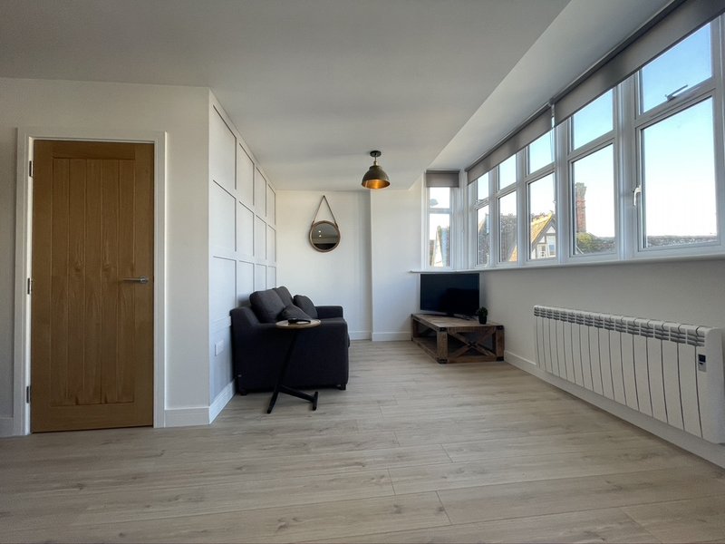 Bright living room with black armchair, TV stand, wooden flooring and large windows