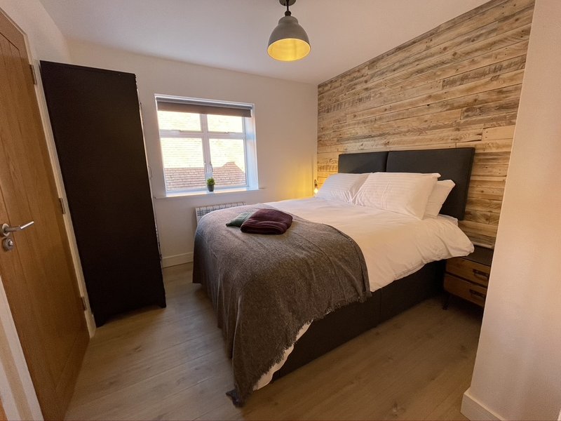 Modern bedroom with double bed, wooden feature wall, window and pendant light