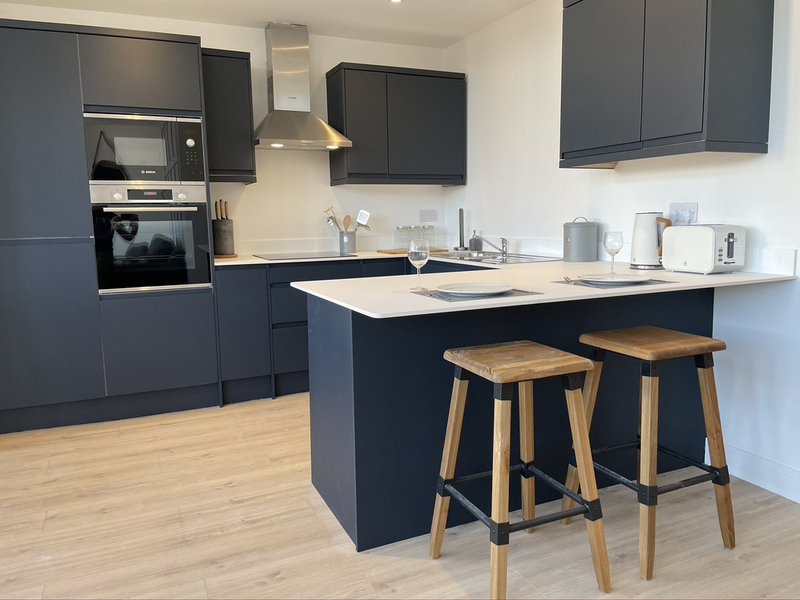 Modern kitchen with dark cabinetry, island with wooden stools, and white countertops