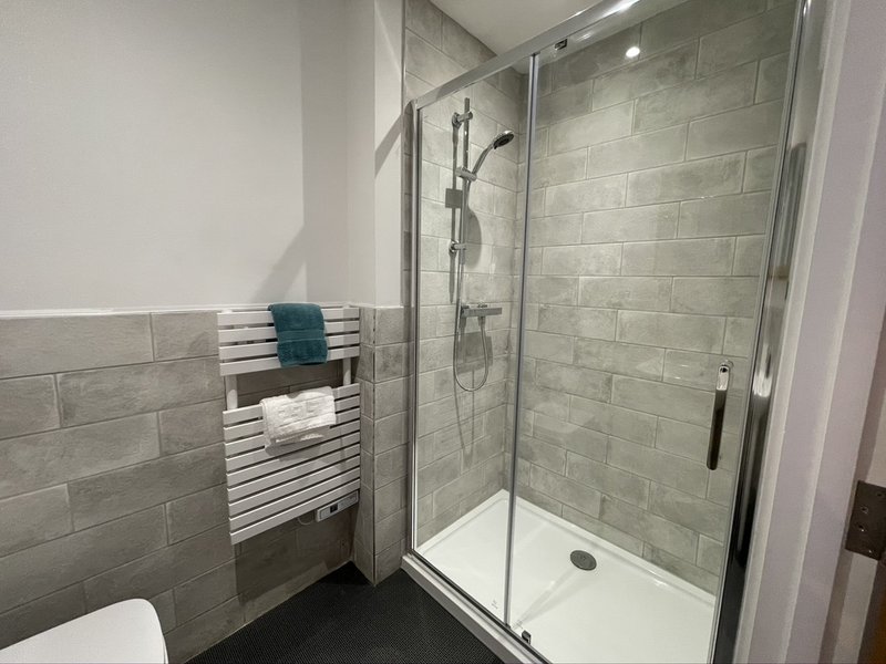 Modern bathroom with walk-in shower, white towel rail, and grey brick tiling