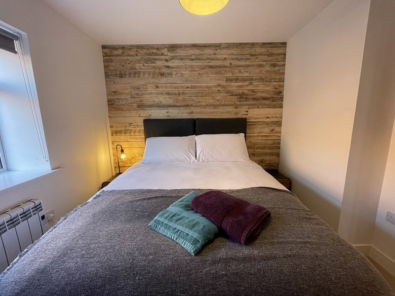 Bedroom with double bed, wooden headboard, gray bedding, and colorful cushions