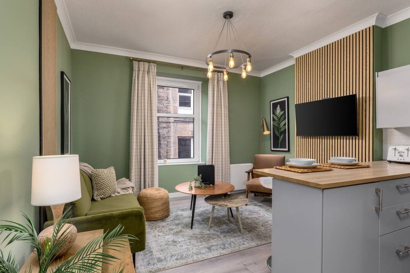 Modern living room with green walls, green sofa, wooden coffee table, and mounted TV