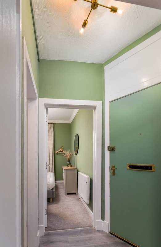 Hallway with green walls, white trim, brass ceiling fixture, and view into bathroom