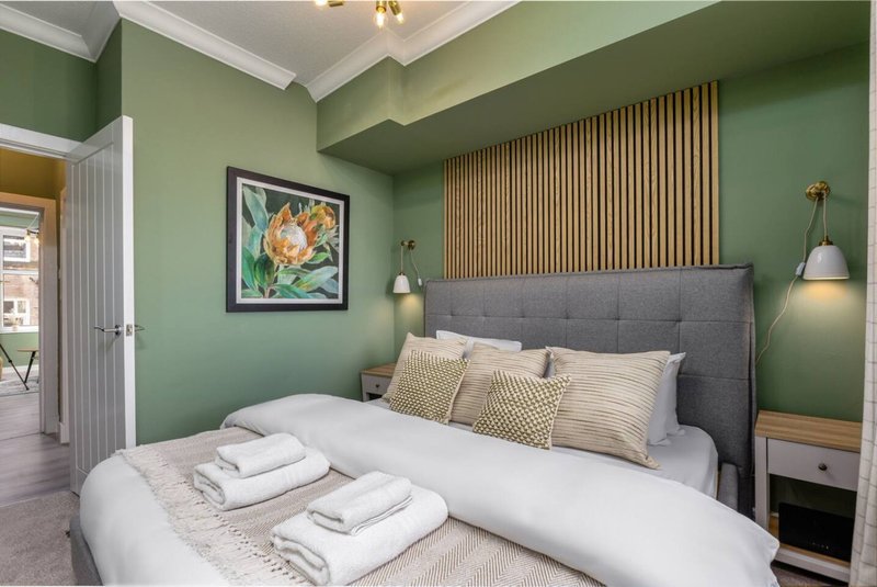 Modern bedroom with green walls, grey upholstered bed, white bedding and decorative pillows