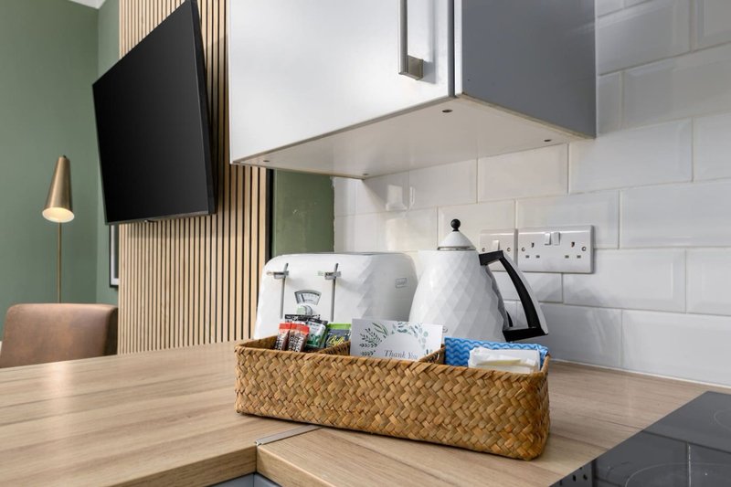 Modern bedroom with wall-mounted TV, green accent wall, wooden desk and wicker storage basket