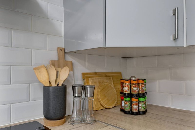 Modern kitchen counter with white subway tile backsplash, wooden utensils, glasses, cutting boards and jarred goods