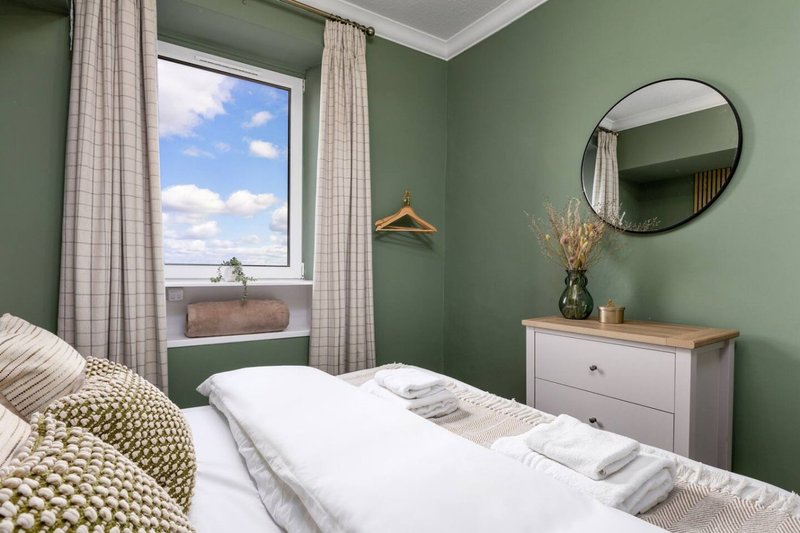 Bright bedroom with double bed, green walls, round mirror and window with countryside view