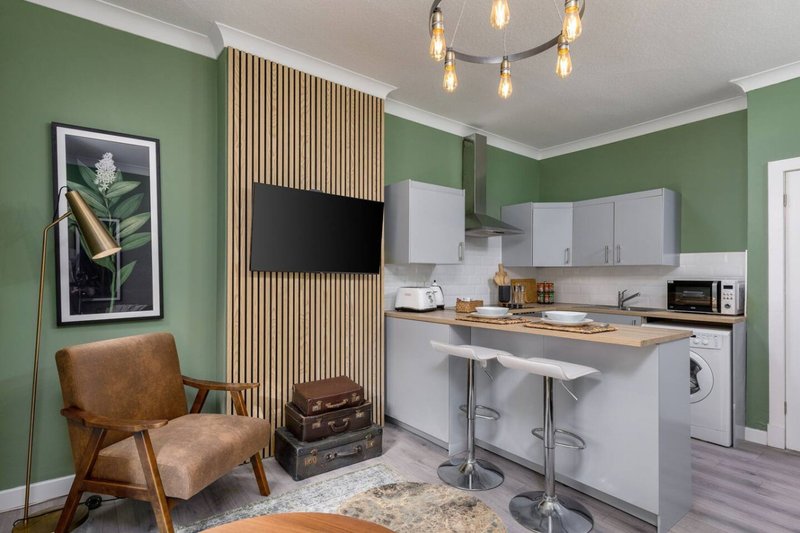 Open-plan studio with green walls, kitchenette, leather armchair, and pendant lighting