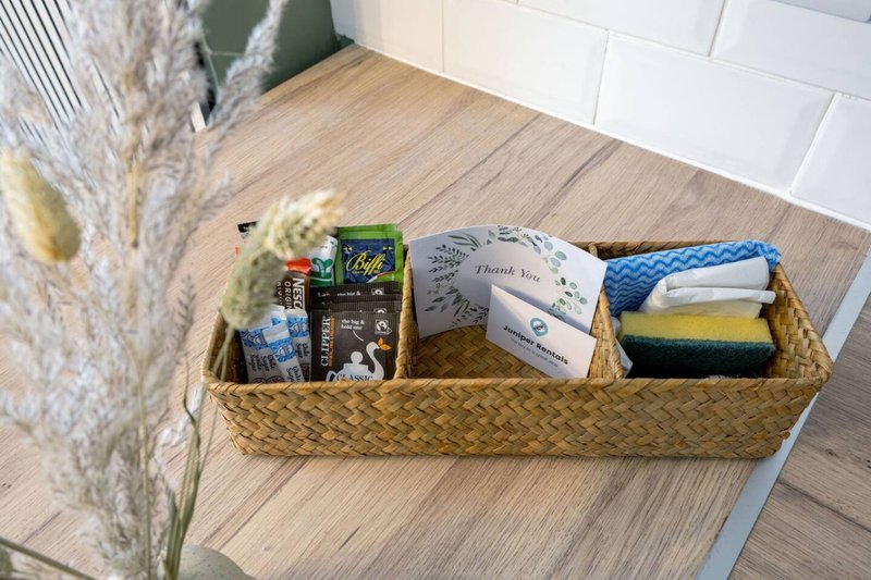 Woven basket on wooden floor containing toiletries, cleaning supplies and welcome items