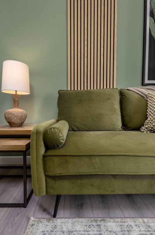 Modern living room with olive green sofa, wooden side table, textured lamp and vertical wall paneling
