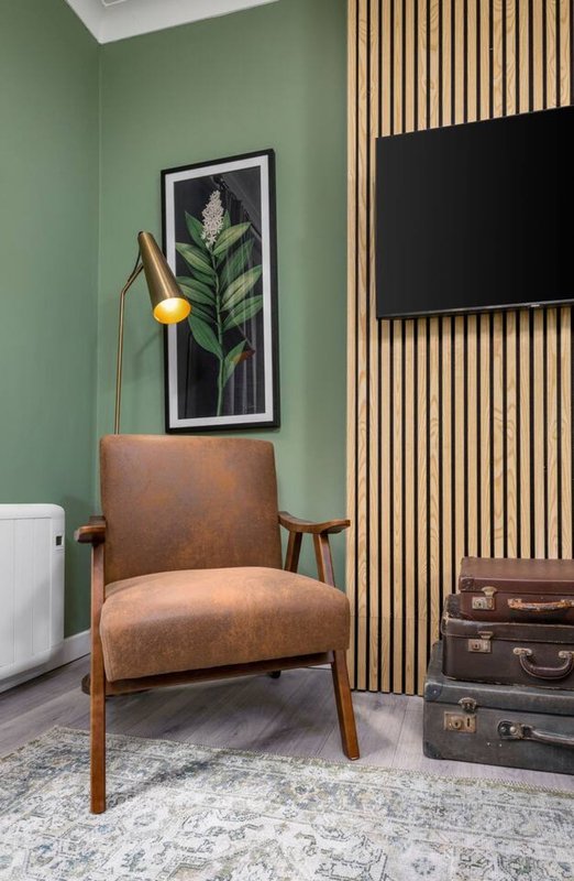 Modern living room with tan leather armchair, green walls, framed botanical print, and wooden slat accent wall