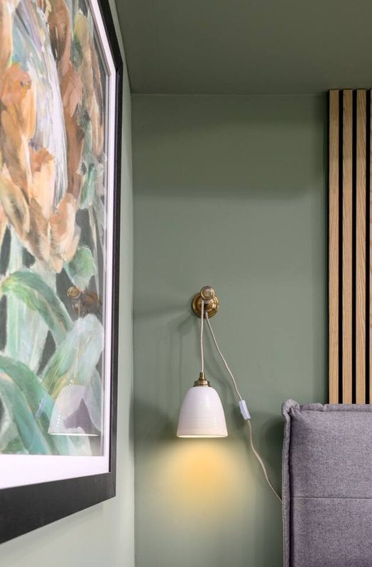 Modern bedroom corner with sage green wall, pendant lamp, framed artwork and upholstered chair