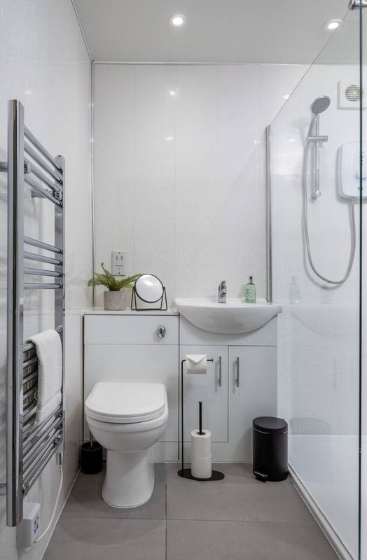 Modern bathroom with white toilet, curved sink vanity, shower enclosure and heated towel rail