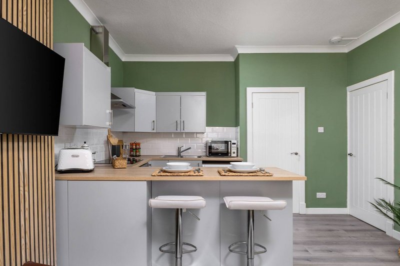 Modern kitchen with green walls, white cabinetry, wooden countertop, island seating, and stainless steel appliances