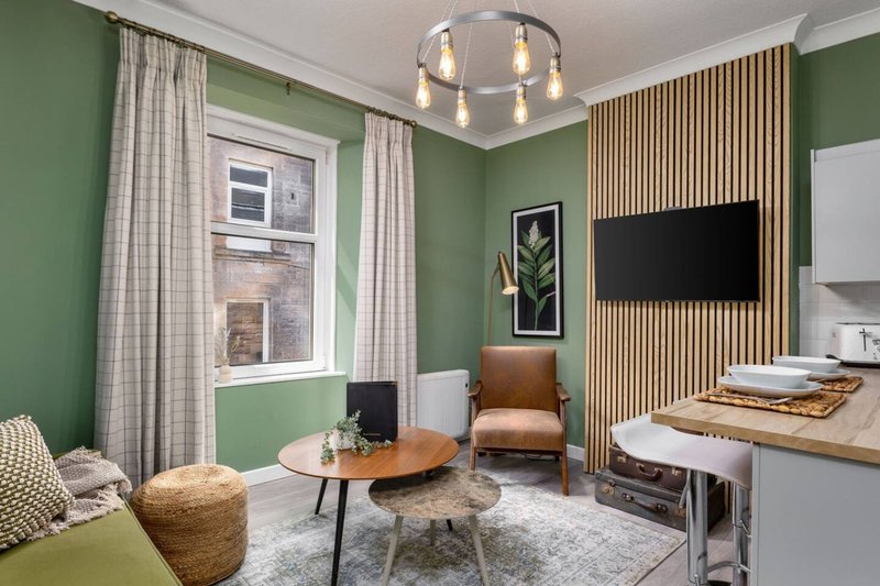 Modern living room with green walls, wooden furniture, wall-mounted TV and pendant lighting