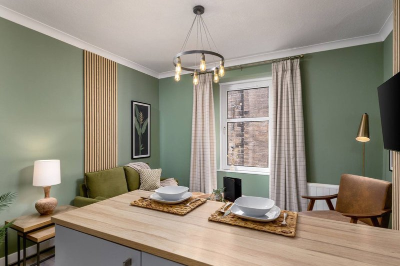 Modern home office with sage green walls, wooden desk, pendant lighting and upholstered chair