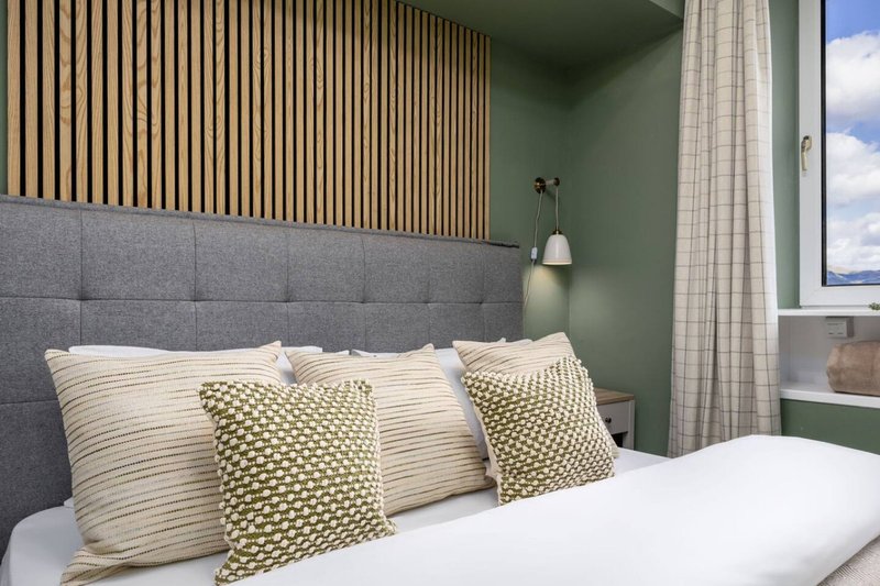 Modern bedroom with grey upholstered headboard, white bedding, patterned pillows and pendant light