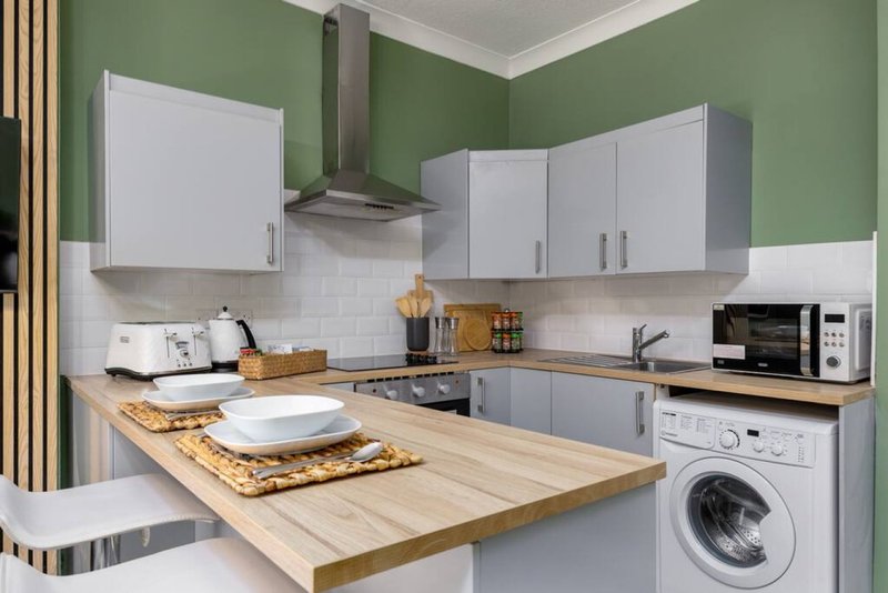 Modern kitchen with green walls, white cabinetry, wooden countertop island and integrated washing machine