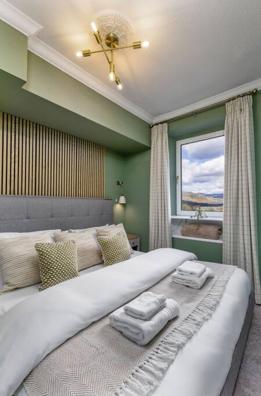 Modern bedroom with double bed, green walls, brass ceiling light, and mountain view through window