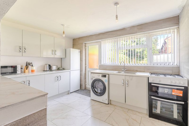 Bright kitchen with white cabinetry, washing machine, electric oven, and large windows