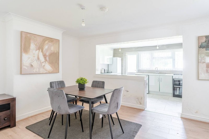 Open-plan dining and kitchen area with wooden table, grey upholstered chairs, and modern kitchen visible through open doorway
