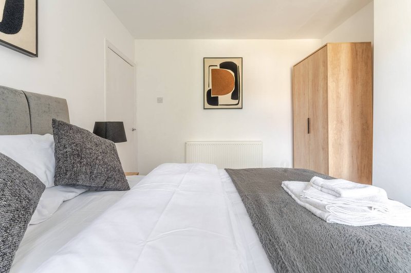 Bright bedroom with double bed, grey bedding, cushions, wooden wardrobe and wall art