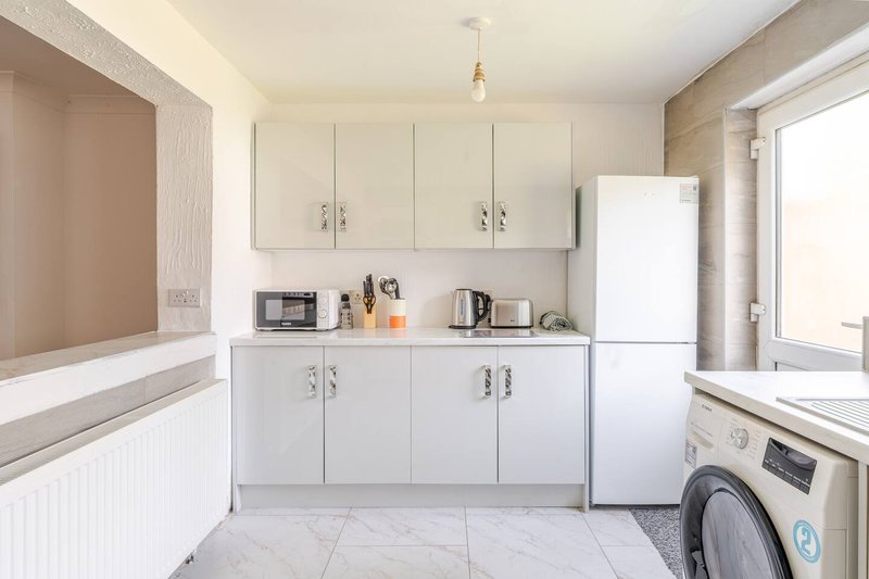 Modern kitchen with white cabinetry, microwave, kettle, washing machine and marble-effect flooring