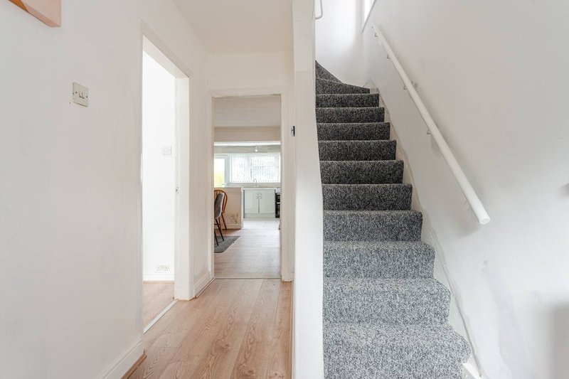 Bright hallway with wooden flooring, white walls, stairs with grey carpet, and white handrail