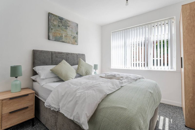 Bright bedroom with double bed, grey headboard, white bedding, wooden nightstand and vertical blinds