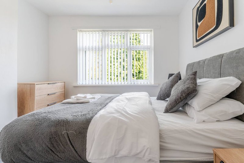 Bright modern bedroom with double bed, grey headboard, white bedding and vertical blinds window