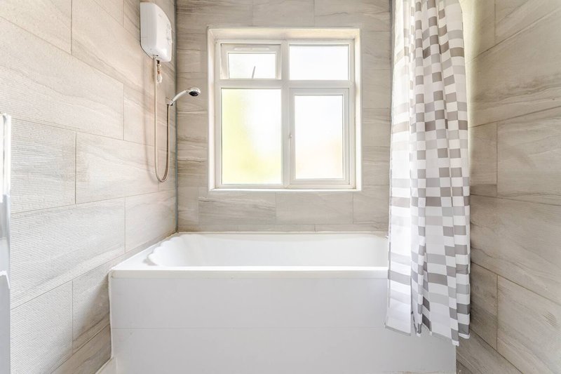 Modern bathroom with white bathtub, tiled walls, window and shower curtain