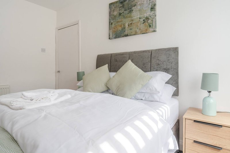 Bright bedroom with double bed, grey upholstered headboard, white bedding, wooden nightstand and mint lamp