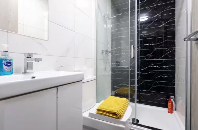 Modern bathroom with white vanity, sink, black marble shower enclosure and yellow towels