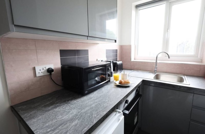 Modern kitchen with black cabinets, gray countertop, pink tile backsplash and window