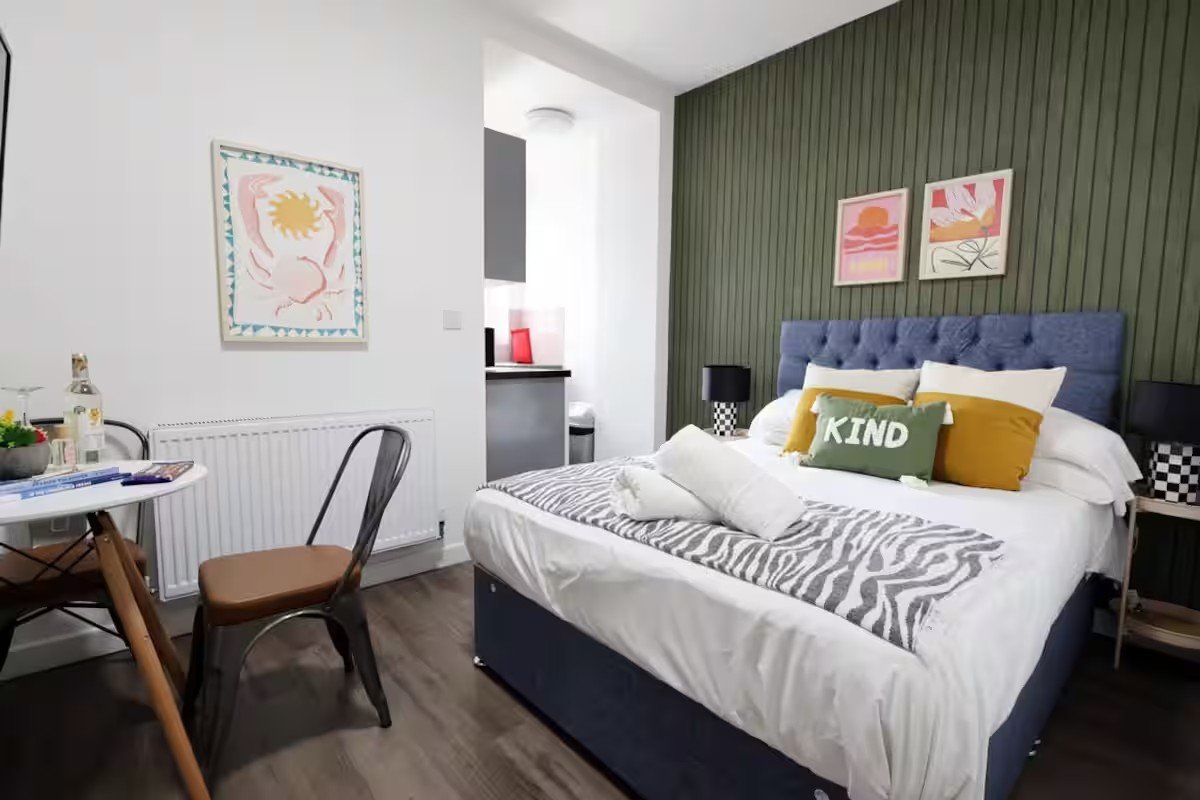 Modern bedroom with blue upholstered bed, green accent wall, desk, and colorful wall art