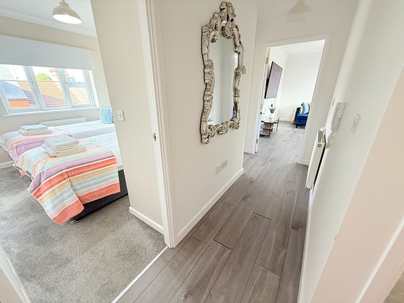 Hallway with wooden flooring leading to bedroom with colorful bedding and window