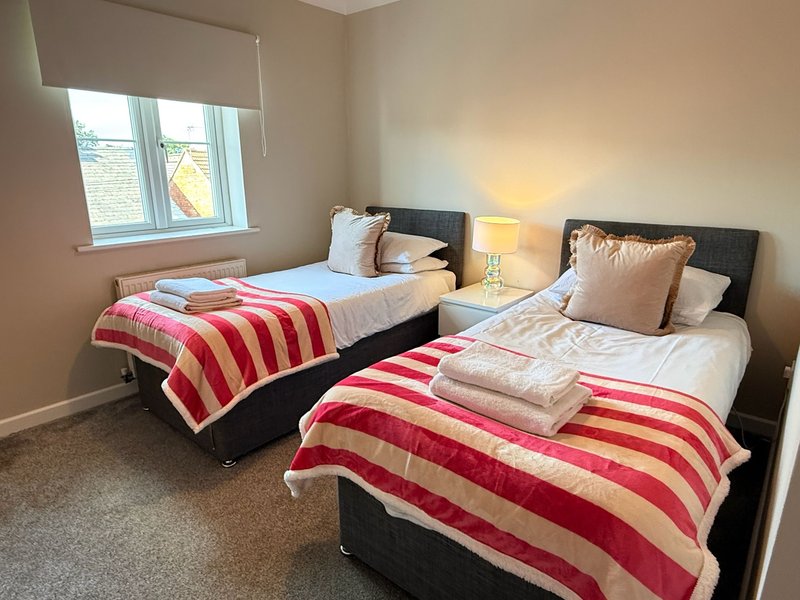 Twin bedroom with two single beds, striped red and yellow blankets, bedside lamp and window
