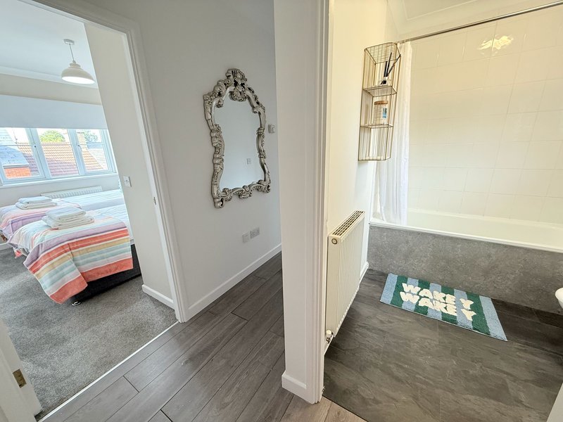 Hallway with dark wood flooring, white doors, decorative mirror and view into bedroom and bathroom