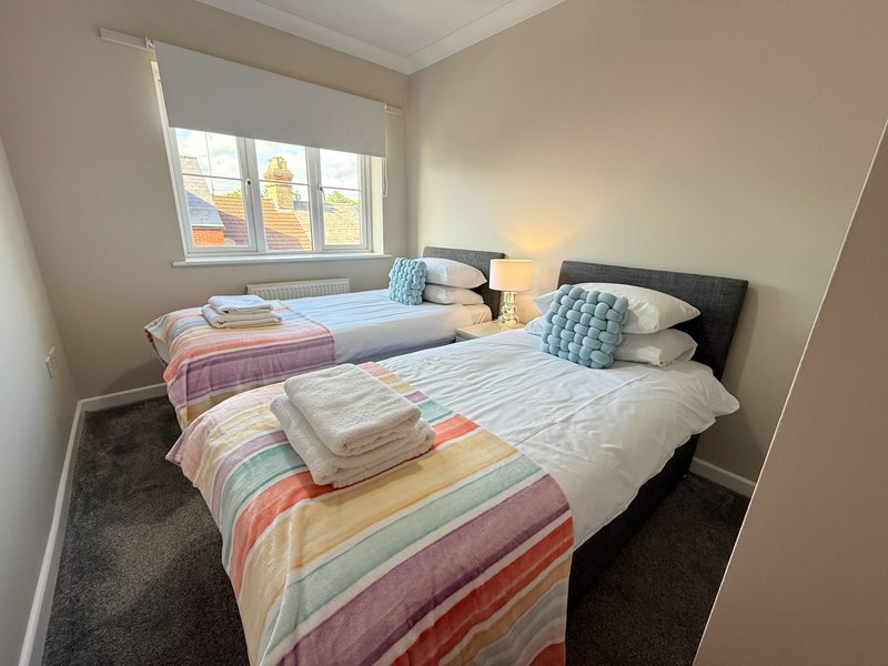 Bright twin bedroom with two single beds, colorful striped bedding, window with blinds, and lamp