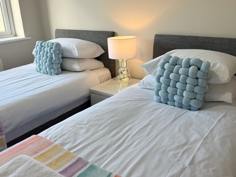 Twin bedroom with two beds, blue quilted cushions, bedside lamp and window
