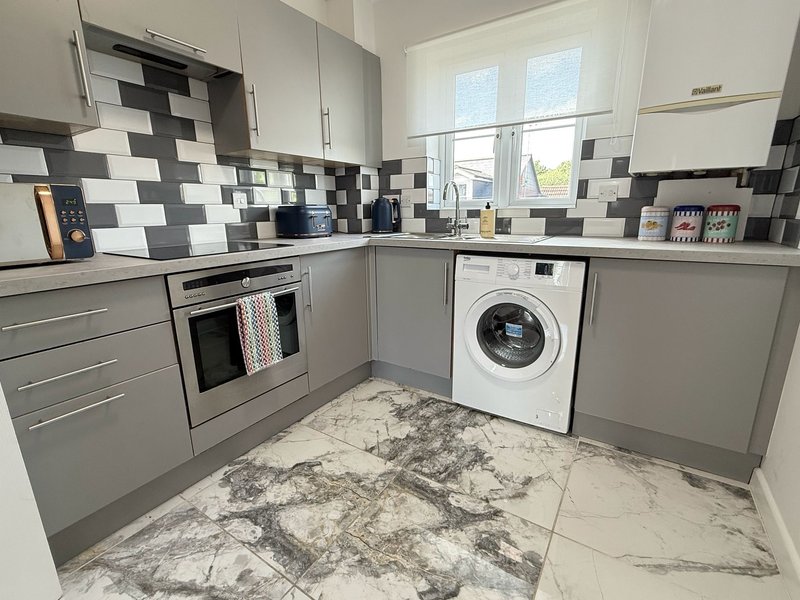 Modern kitchen with grey cabinetry, black and white tile backsplash, marble flooring and integrated appliances