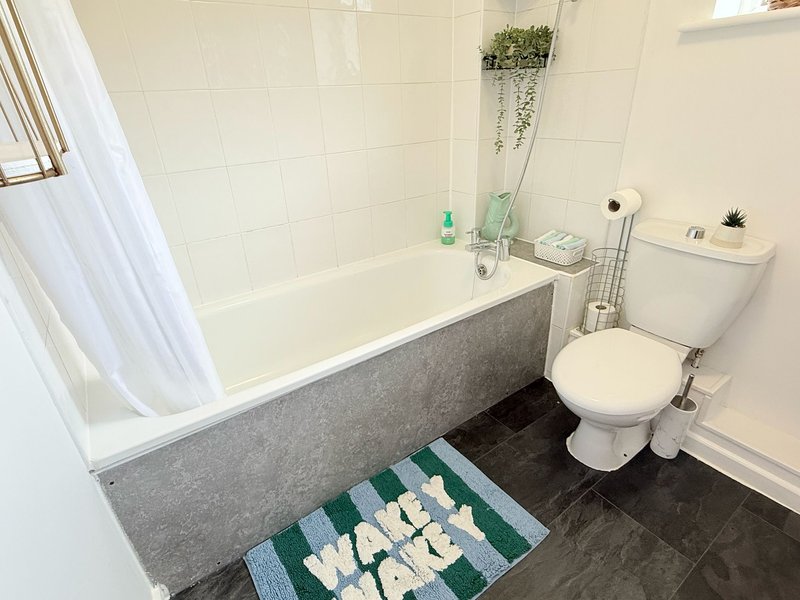 Bathroom with bathtub, toilet, sink, tiled walls and dark floor with bath mat