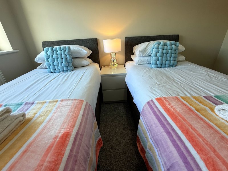 Twin bedroom with two single beds, blue cushions, striped blankets, and bedside lamp