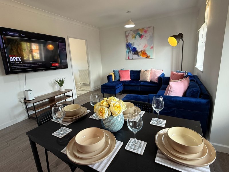 Open-plan living and dining area with blue velvet sofa, dining table set for two, and wall-mounted TV