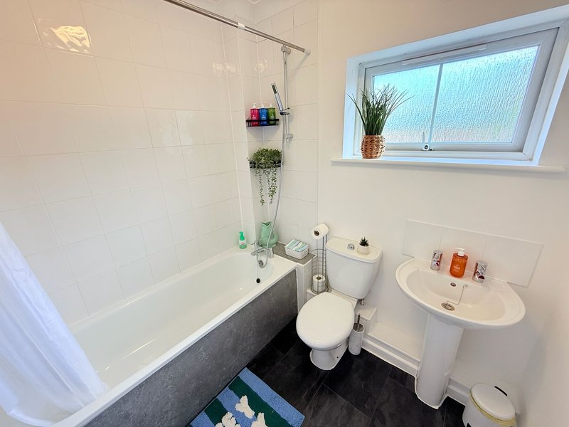 Clean bathroom with bathtub, toilet, sink, window and toiletries on shelves