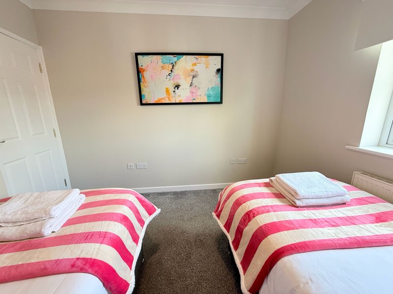 Bedroom with two single beds, pink and white striped bedding, abstract wall art